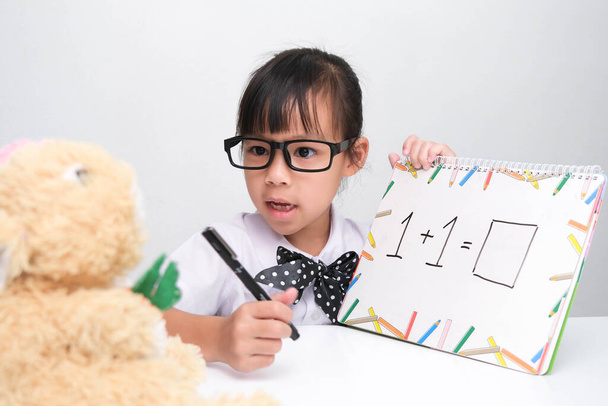 Cute Asian little girl gra nauczyciel gra roli. Mała dziewczynka uczy matematyki swojego przyjaciela misia. Nauka i zabawa dla dzieci w domu. - Zdjęcie, obraz