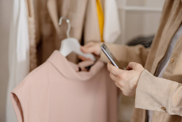 Kobieta trzyma smartfona i robi zdjęcia swoich starych ubrań, żeby je sprzedać online. Sprzedam na stronie internetowej, e-commerce. Ponowne użycie, używana koncepcja. Świadomy konsument, zrównoważony styl życia. Widok z bliska - Zdjęcie, obraz
