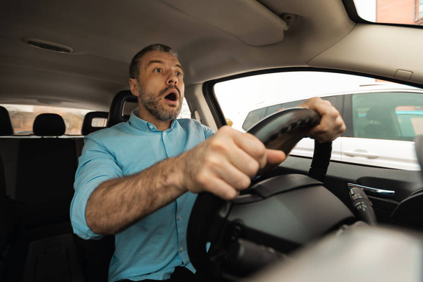 Πορτρέτο του φοβισμένος άνθρωπος οδήγηση αυτοκινήτου σε υψηλή ταχύτητα και επέζησε από ένα ατύχημα. Αντίδραση Σοκ. Εκπληκτικός τύπος που λαχανιάζει, κοιτάζει συντριβή ή ζώο στο δρόμο με ανοιχτό στόμα, θέα στο παρμπρίζ - Φωτογραφία, εικόνα