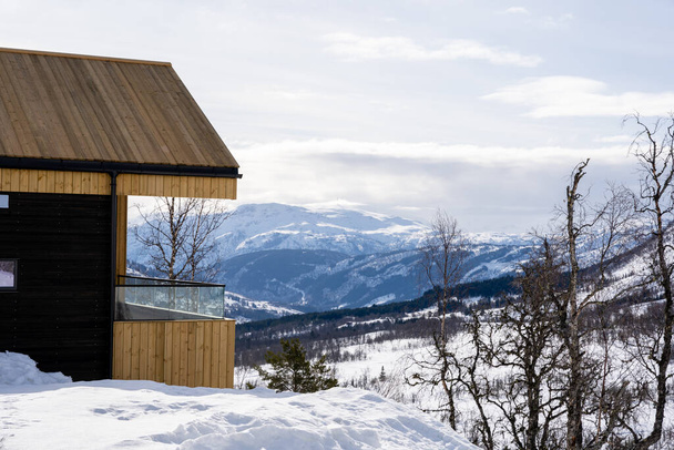 Kışın Norveç 'in dağlarında ahşap bir tatil evi. Güzel mavi gökyüzünde bir sürü beyaz kar ve tüylü beyaz bulutlar var. - Fotoğraf, Görsel