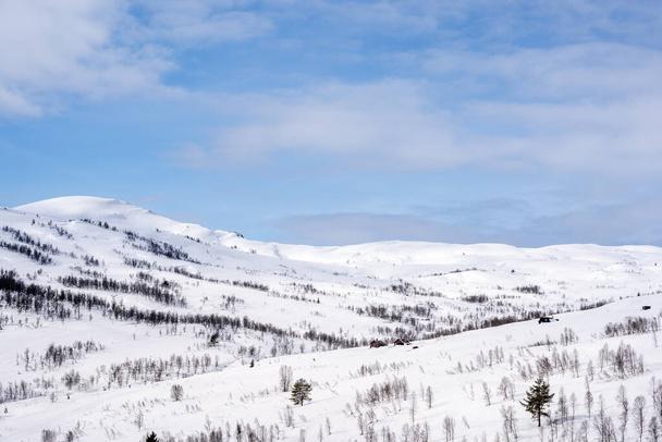 Białe ośnieżone góry w Norwegii, nad którymi jest błękitne niebo z miękkimi chmurami - Zdjęcie, obraz