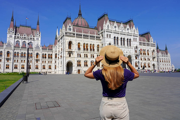 Holidays in Budapest. Back view of beautiful stylish girl enjoying view of Hungarian Parliament Building in Budapest, Hungary. Tourism in Europe. - Photo, Image