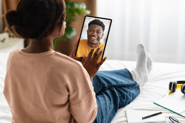 Rückansicht der schwarzen Frau mit digitalem Tablet, Videotelefonie mit ihrem Liebhaber, Sitzen im modernen Schlafzimmer zu Hause, selektiver Fokus auf Pad. Mobile App-Werbung, Collage, Kopierraum - Foto, Bild