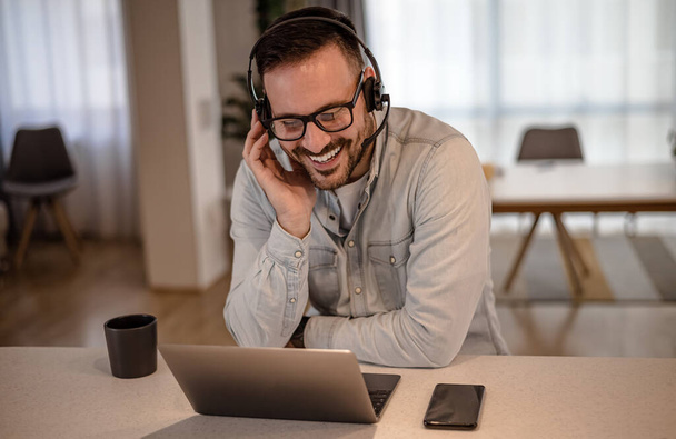 Cheerful young adult businessman entrepreneur freelancer making online video call and telecommuting. Portrait of man telecommuting working from home office providing call support call center operator. - Φωτογραφία, εικόνα