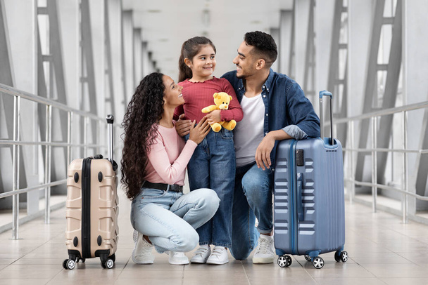 Viaje de vacaciones. Retrato de padres árabes felices y linda hijita relajándose en el aeropuerto mientras esperan su vuelo, alegre familia de Oriente Medio que se une, disfrutando de los próximos viajes - Foto, imagen