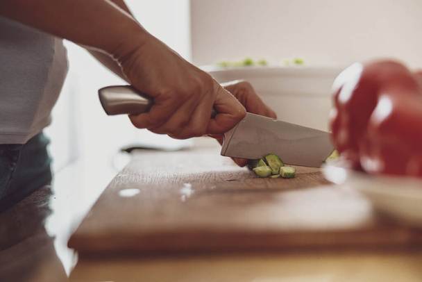 Zöldségszeletelés közelkép egy késsel a konyhaasztalon - Fotó, kép