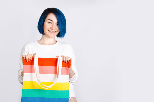 Female with blue hair holding a rainbow bag on a white background. LGBT flag colors. - Foto, imagen