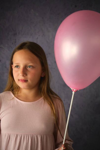 studio portrait of a girl with a pink balloon in her hand on a dark background - Fotó, kép