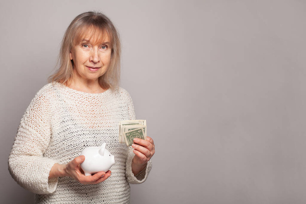 volwassen vrouw met amerikaanse dollars en spaarvarken bank tegen witte achtergrond met kopieerruimte - Foto, afbeelding