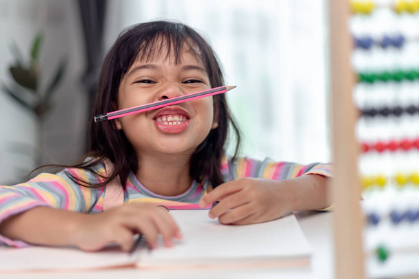 grappig meisje spelen houden pen tussen neus en lippen als snor kijken naar de camera, speels verveeld na het leren van lange uren. - Foto, afbeelding