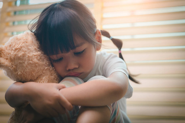 Nahaufnahme einsames kleines Mädchen, das Spielzeug umarmt, allein zu Hause sitzt, unglückliches Kind, das auf Eltern wartet, über Probleme nachdenkt, schlechte Beziehung in der Familie, psychologisches Trauma - Foto, Bild
