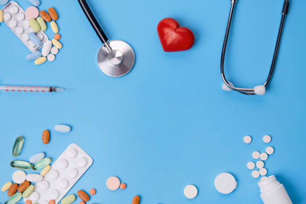 Pillen, vitaminen en wegwerpspuit, hart, stethoscoop op blauwe achtergrond bovenaanzicht Ruimte voor tekst. zie arts. - Foto, afbeelding