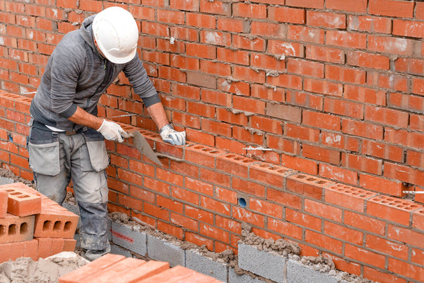 Bricklayer laying bricks on mortar on new residential house construction - Photo, Image