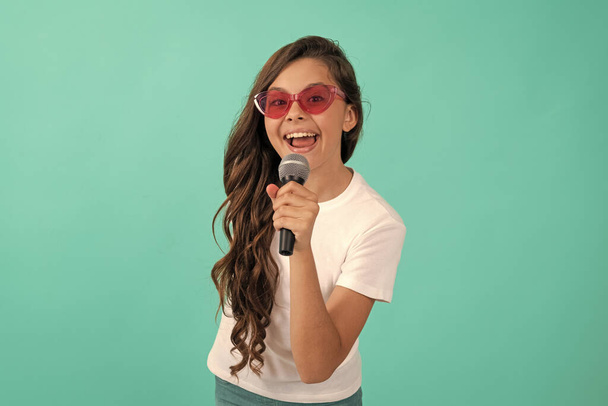 A zene az, ami vagyok. Boldog gyermek énekel. Karaoke és élő zene. Női énekes tartja mikrofon kék háttér. Hagyd, hogy énekelj.. - Fotó, kép