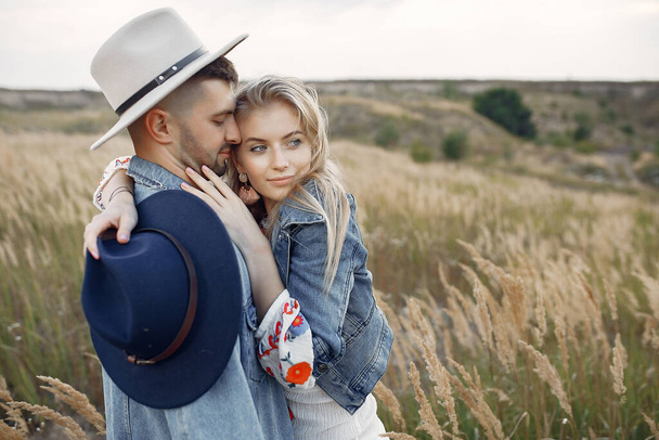 Loving couple in a wheat field. Beautiful blonde in a blue hat. - Фото, изображение