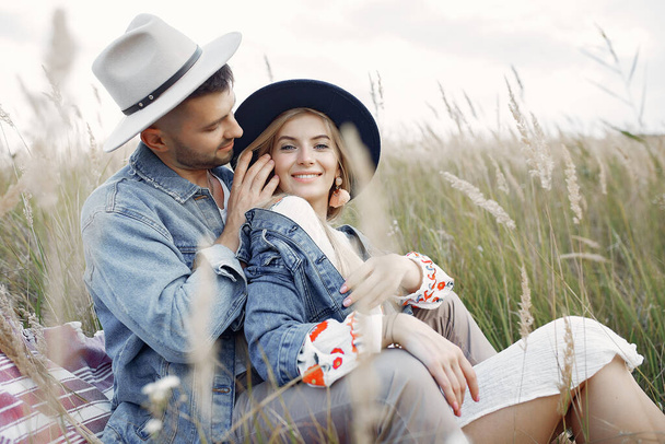 Loving couple in a wheat field. Beautiful blonde with her boyfrinds. They sitting on a blanket - Фото, изображение