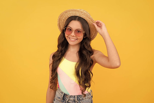 happy teen girl in summer straw hat and glasses has curly hair on yellow background, fashion. - Foto, imagen