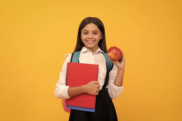 Happy girl child smile holding apple and books yellow background, school. - Photo, image