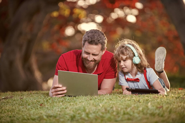 happy family of father and son use laptop for video call or lesson listen music in headphones in park, family blog. - Photo, Image