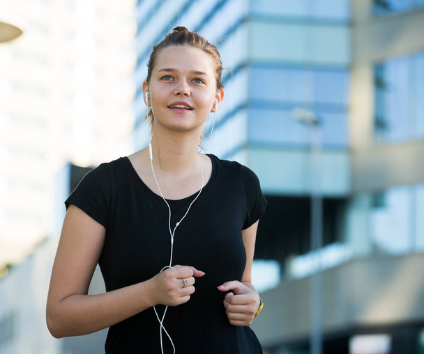 Young girl in black listening to music enjoying morning run outdoors - Valokuva, kuva