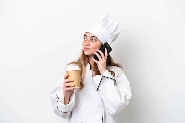 Молода кавказька шеф-кухарка ізольована на білому тлі, тримає каву, щоб забрати і мобільний
 - Фото, зображення