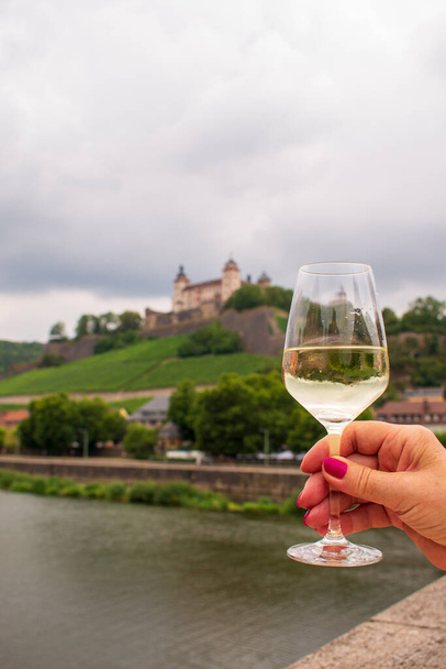 Eine Frau hält ein Glas Weißwein auf einer Alten Mainbrücke vor der Festung Marienberg auf einem Weinberg in der bayerischen Touristenstadt   - Foto, Bild