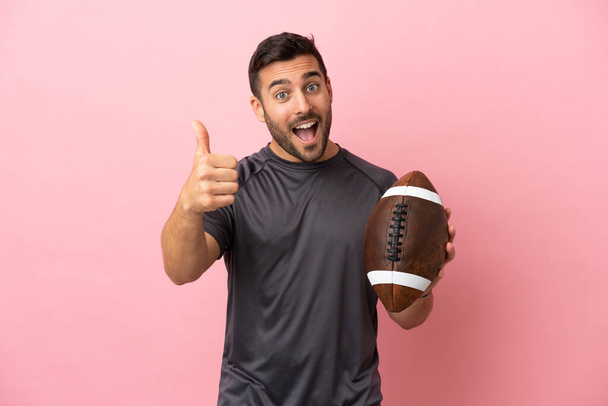 Young caucasian man playing rugby isolated on pink background with thumbs up because something good has happened - 写真・画像