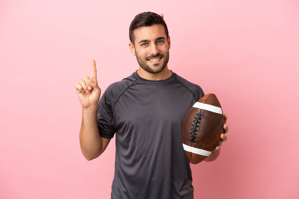 Junger kaukasischer Mann spielt Rugby isoliert auf rosa Hintergrund zeigt und hebt einen Finger im Zeichen der besten - Foto, Bild
