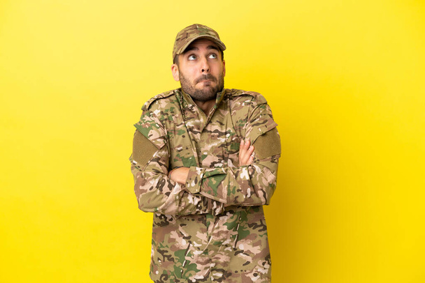 Military man isolated on yellow background making doubts gesture while lifting the shoulders - Photo, image