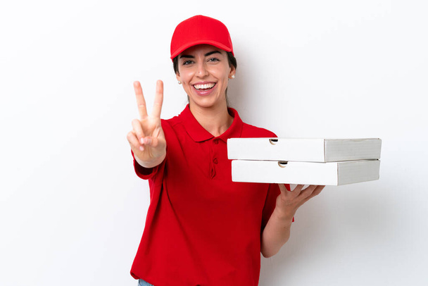 Entrega de pizza mujer caucásica con uniforme de trabajo recogiendo cajas de pizza aisladas sobre fondo blanco sonriendo y mostrando signo de victoria - Foto, Imagen