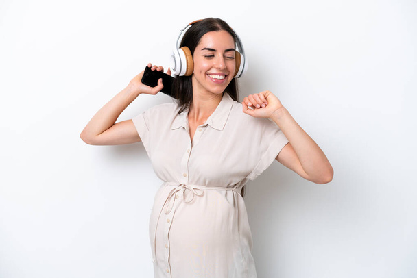 Joven mujer caucásica aislada sobre fondo blanco embarazada y bailando mientras escucha música - Foto, imagen