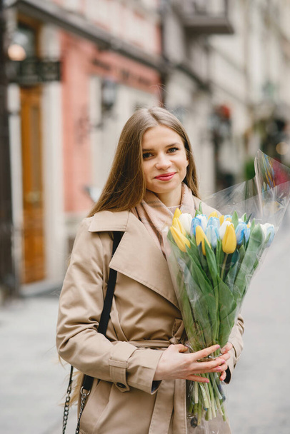 Beautiful girl in a brown coat. Woman in a spring city. Lady with bouquet of flowers - Foto, immagini