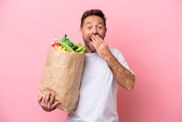 Homme du moyen âge tenant un sac d'épicerie isolé sur fond rose bouche de couverture heureuse et souriante avec la main - Photo, image