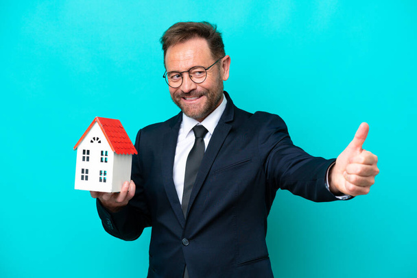 Real estate middelbare leeftijd agent man geïsoleerd op blauwe achtergrond geven van een duim omhoog gebaar - Foto, afbeelding
