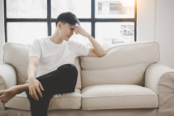 Λυπημένος δυστυχισμένος όμορφος Ασιάτης κάθεται στον καναπέ και κρατάει το μέτωπο ενώ έχει πονοκέφαλο αναστατωμένος νεαρός άνδρας νιώθει κατάθλιψη στενοχωρημένος με προβλήματα σχέσεων ζωής υποφέρει από ψυχολογικά ή ψυχολογικά προβλήματα - Φωτογραφία, εικόνα