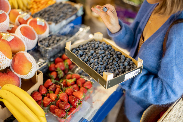 Woman holds box full of blueberries, while buying fresh food at local market, cropped view focused on berries - Photo, Image