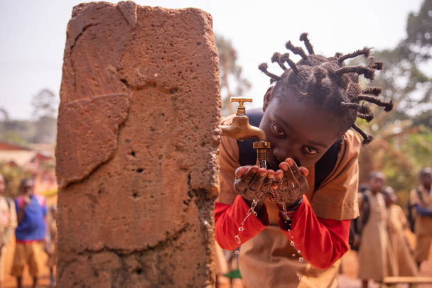 Mała czarna dziewczynka zaspokaja swoje pragnienie wodą płynącą ze szkolnego kranu fontanny. Koncepcja wody w Afryce. - Zdjęcie, obraz