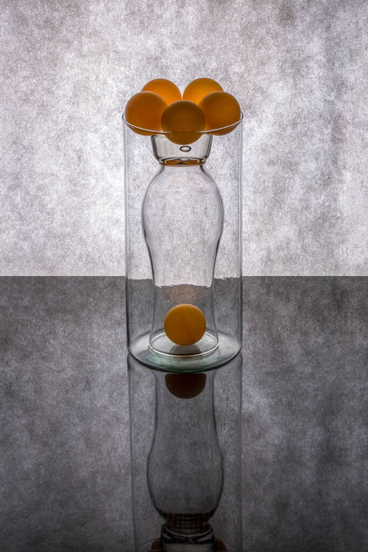 Martwa natura ze szklanymi przedmiotami i pomarańczowymi kulkami - Zdjęcie, obraz