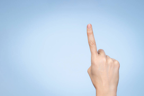Un gesto della mano. La mano femminile mostra il numero uno. Donna che punta con indice su sfondo azzurro. - Foto, immagini