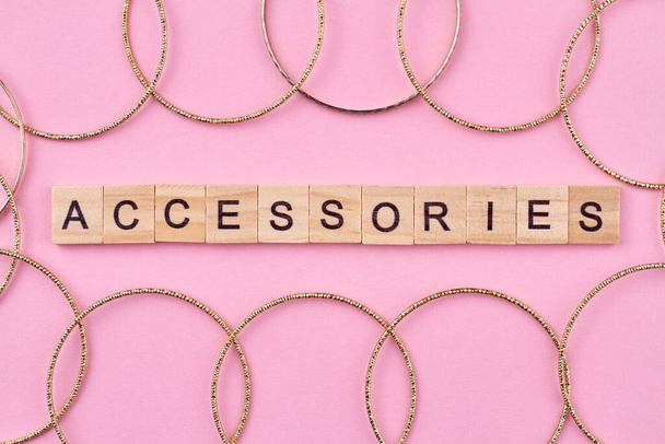 Houten kubussen met geschreven woord accessoires en vele gouden vrouwelijke armbanden. Vrouwen sieraden op roze achtergrond. - Foto, afbeelding