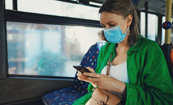 Woman in medical mask with mobile phone in the bus. - Φωτογραφία, εικόνα