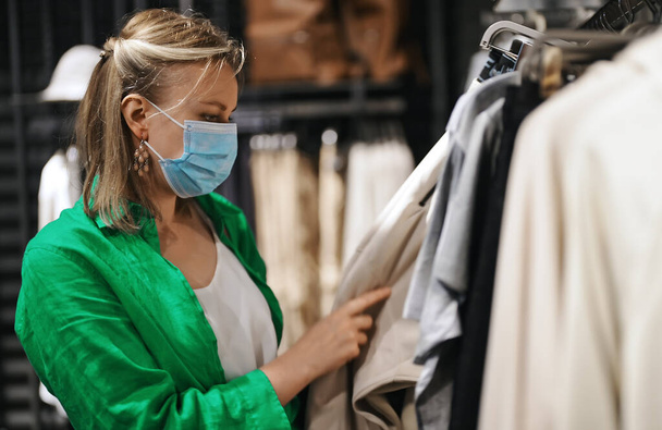 Mujer en máscara médica elegir la ropa en la tienda de outlet. - Foto, imagen