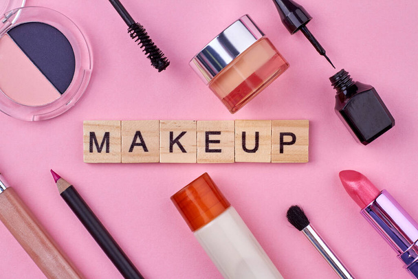 Close-up de vários acessórios de maquiagem feminina no fundo rosa. Cubos de madeira com maquiagem de texto. - Foto, Imagem