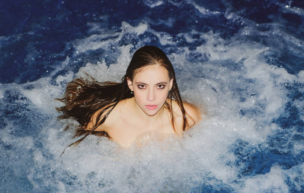 Primer plano de la moda sexy retrato de una chica relajarse en el spa. Mujer posando sobre el fondo azul del agua salpicada. Chica sexy en la piscina. - Foto, imagen
