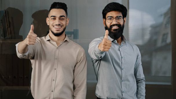 Happy confident men young professional colleagues co-workers partners arabian hispanic business people looking at camera showing thumbs up hand sign gesture recommending best choice positive feedback - Foto, Imagen