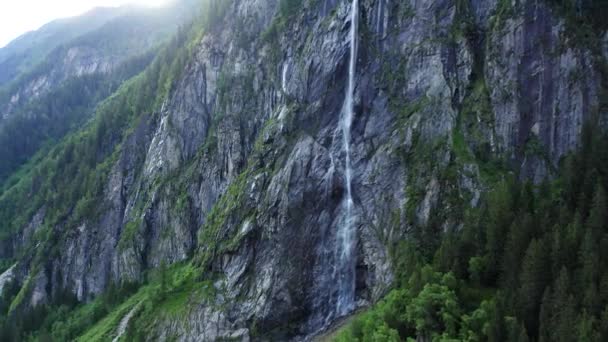 Una poderosa corriente de agua cae de un acantilado, elevando la espuma y el rocío de agua en el aire. La exuberante vegetación verde cubre las laderas de las montañas. - Metraje, vídeo