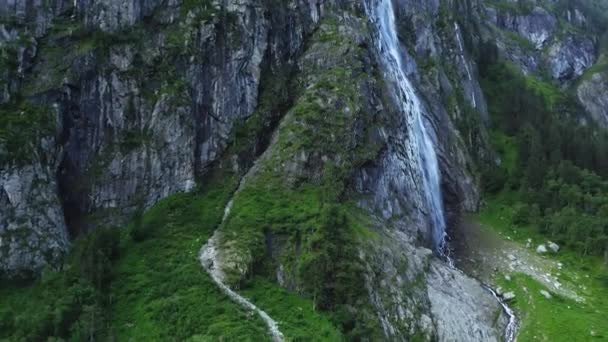 Een krachtige stroom water valt van een klif, waardoor schuim en waterspray in de lucht komen. Weelderige groene vegetatie bedekt de hellingen van de bergen. - Video