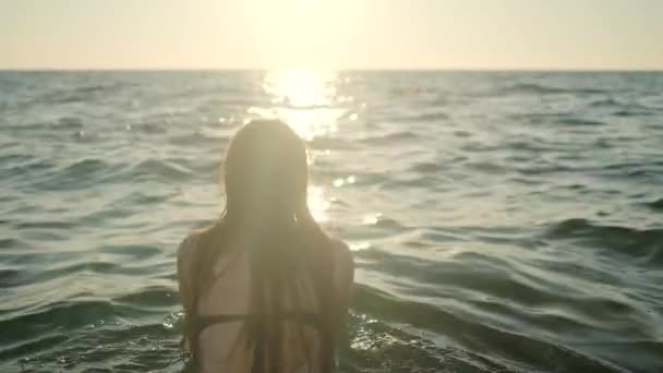 Egy fiatal, bikinis barna nő ugrik és belemerül a gyönyörű tengerbe nyáron este. - Felvétel, videó
