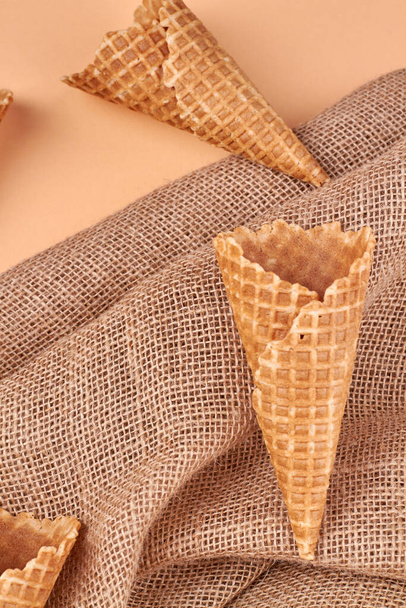 Composition with ice cream waffle cones and sackcloth on color background. Natural food ingredients. - Foto, afbeelding