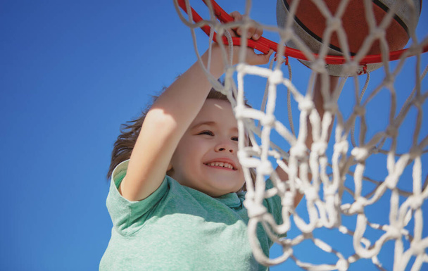 Netter lächelnder Junge spielt Basketball und macht Slam Dunk. Nahaufnahme Porträt eines jungen Basketballspielers - Foto, Bild
